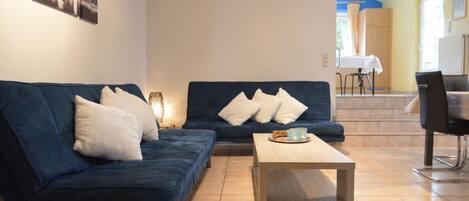 A living room with two blue sofas, a wooden coffee table, and a dining area with a table and chairs.