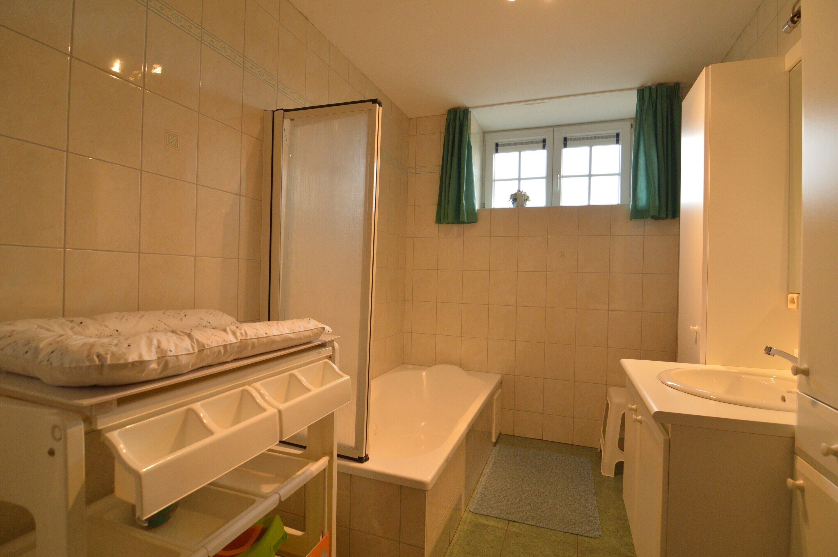 A bathroom with a bathtub, a sink, a mirror, and a window with curtains.