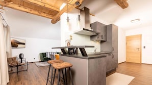 Een moderne keuken met een centraal eiland, barkrukken, een hanglamp en een houten plafond.