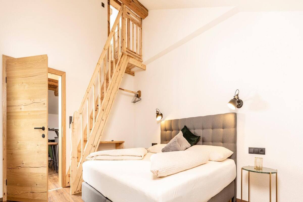 Une chambre avec un escalier en bois, un lit avec des oreillers, une table de chevet et une lampe.