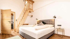 Een slaapkamer met een houten trap, een bed met kussens, een nachtkastje en een lamp.