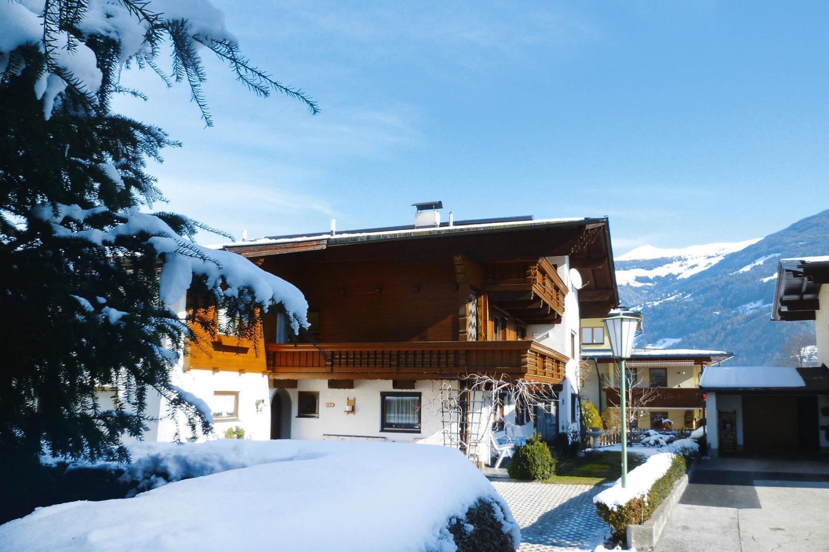 A wooden chalet with a balcony, surrounded by snow-covered trees and mountains.
