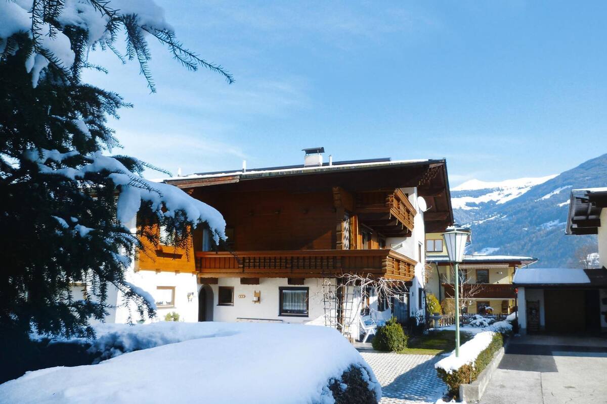 A wooden chalet with a balcony, surrounded by snow-covered trees and mountains.