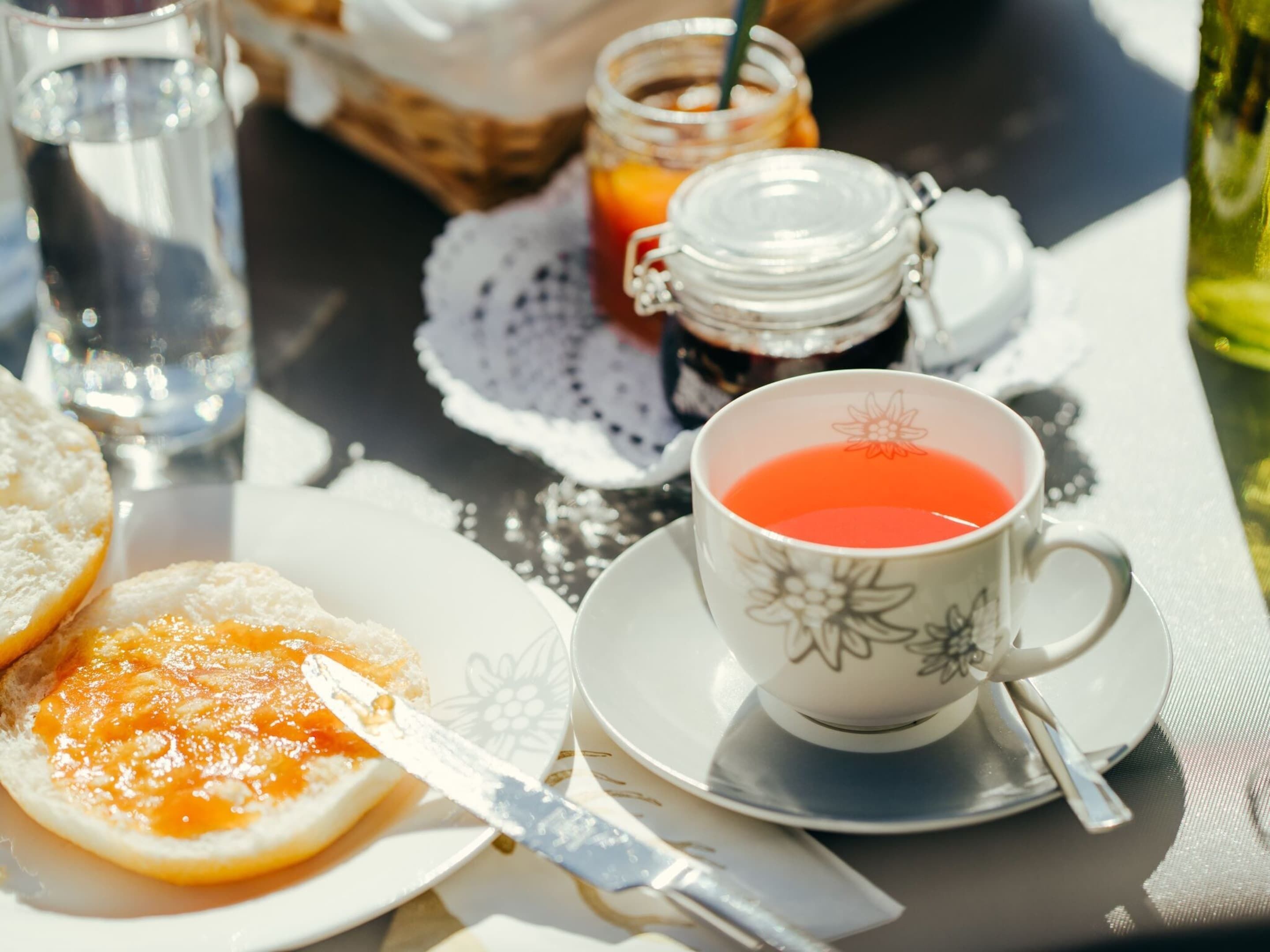 Een tafel met een kop thee, een pot jam, een glas water en een bord met toast.