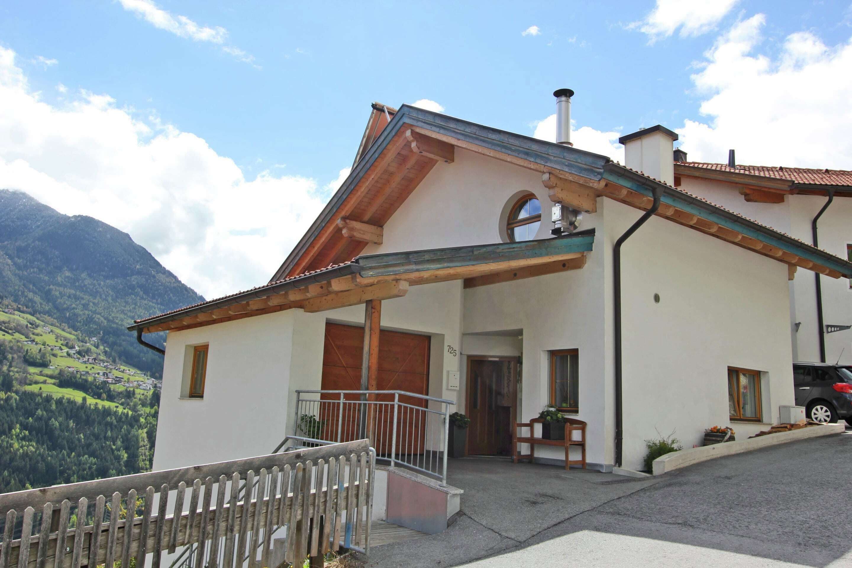 Ein zweistöckiges Haus mit Balkon, einer Holztreppe und Blick auf einen Berg.