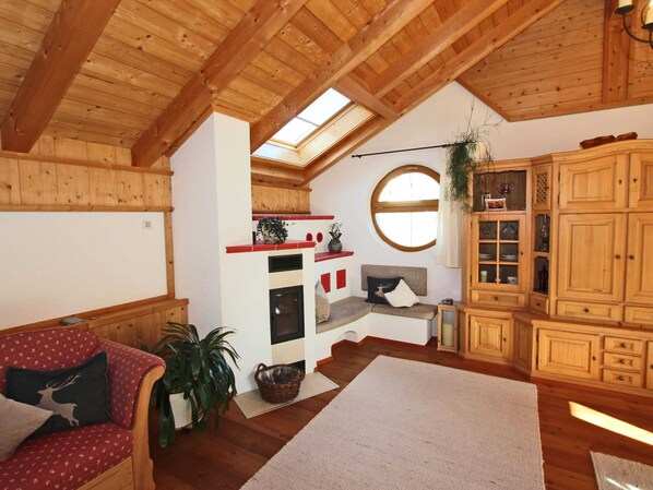 L’intérieur chaleureux d’un chalet avec des poutres en bois, une cheminée, un canapé, un coin repas et une grande armoire en bois.