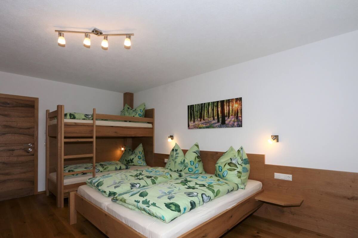 A bunk bed room with a wooden headboard, a painting of a forest, and a ceiling light fixture.