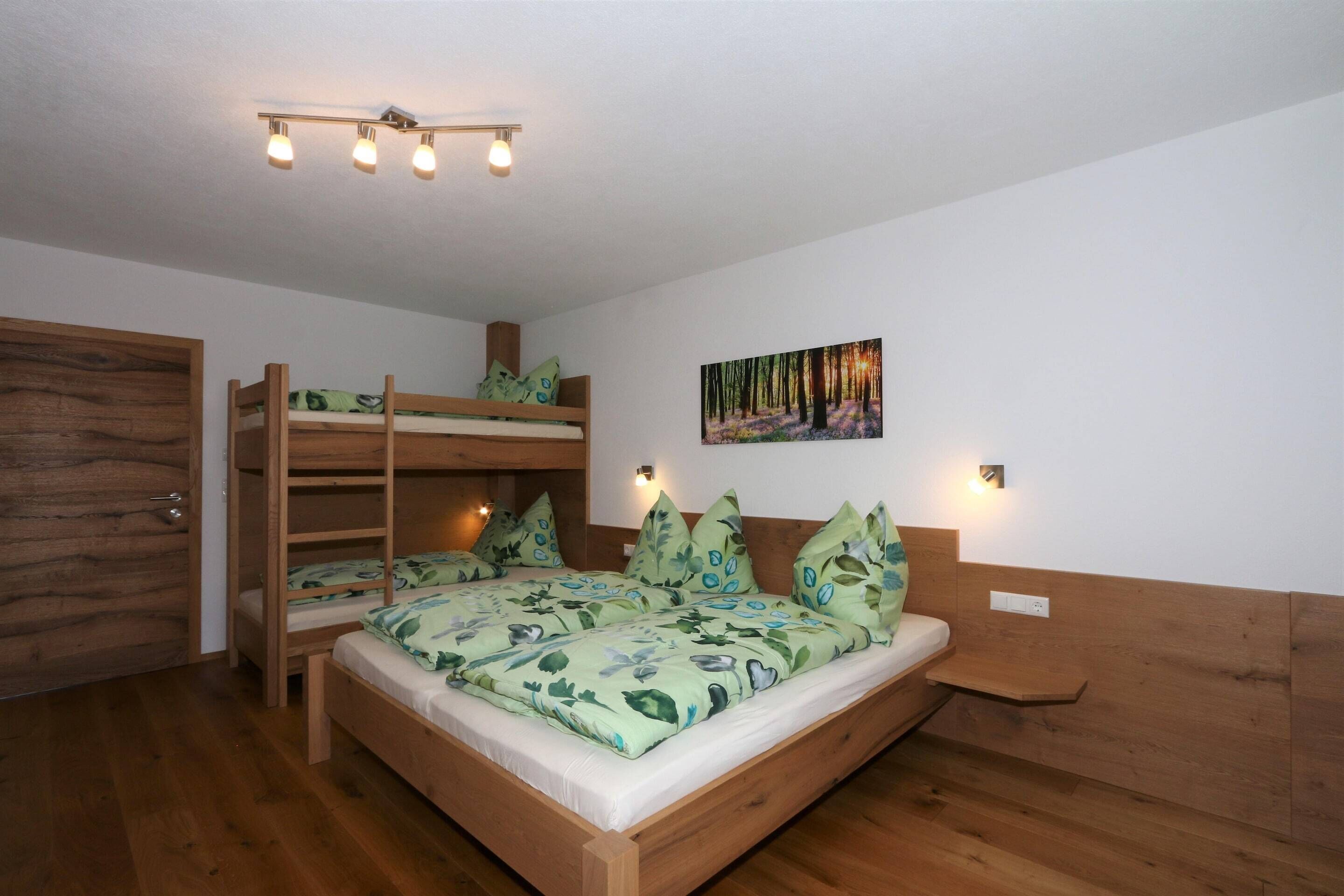A bunk bed with a green floral bedspread, a wooden headboard, and a painting of a forest on the wall.