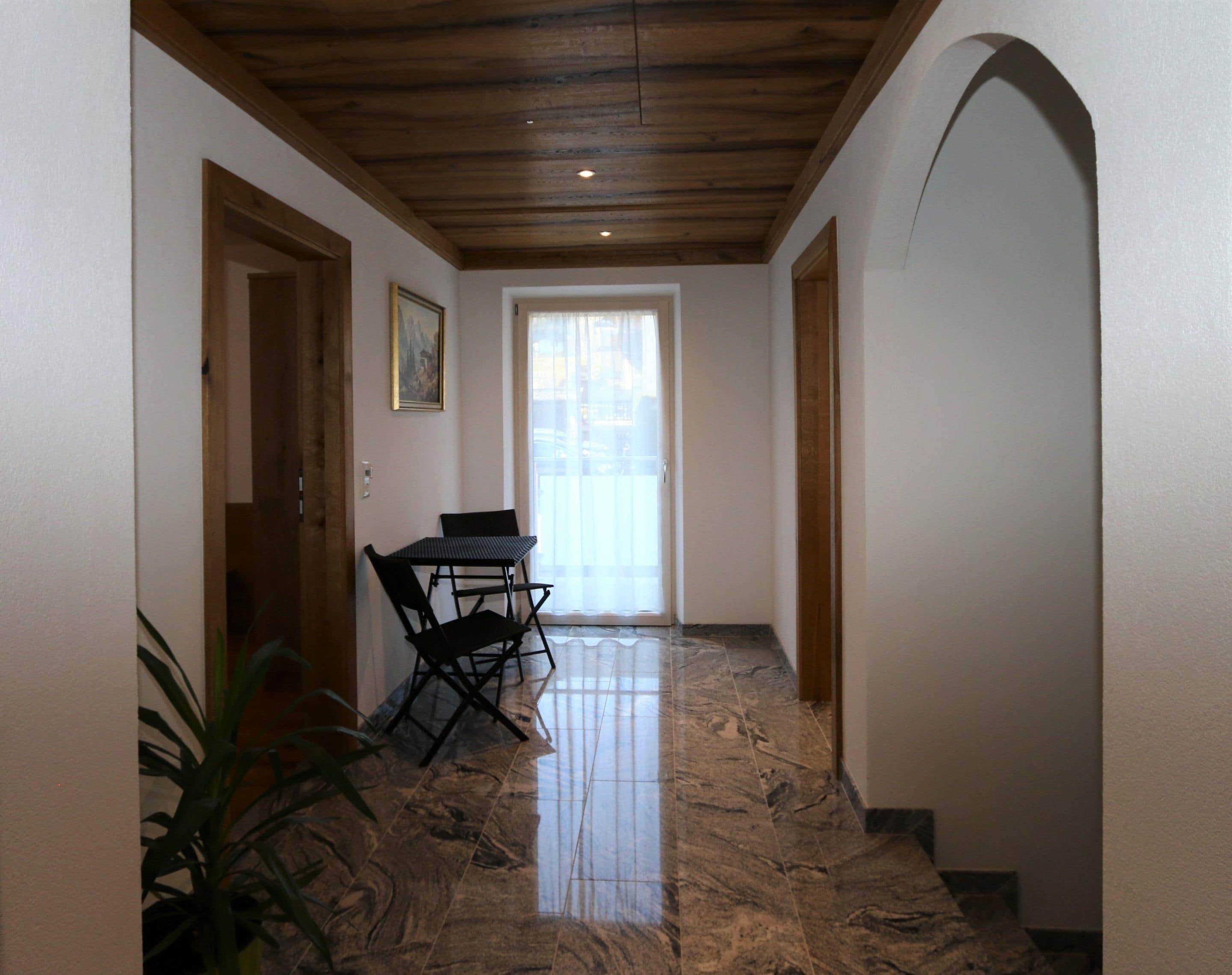 A hallway with a wooden ceiling, a dining table with chairs, and a potted plant.
