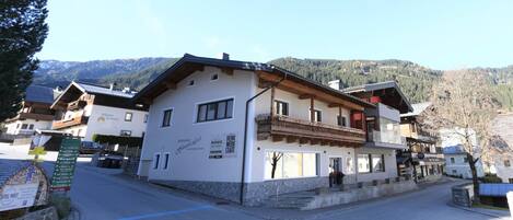A traditional Alpine-style building with a stone base and wooden upper floors, featuring a balcony and signage for local businesses.
