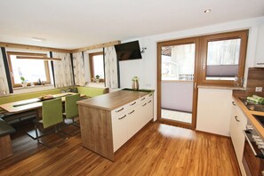 Una cucina moderna con pavimento in legno, un'area pranzo con sedie verdi e un'ampia finestra con tende.