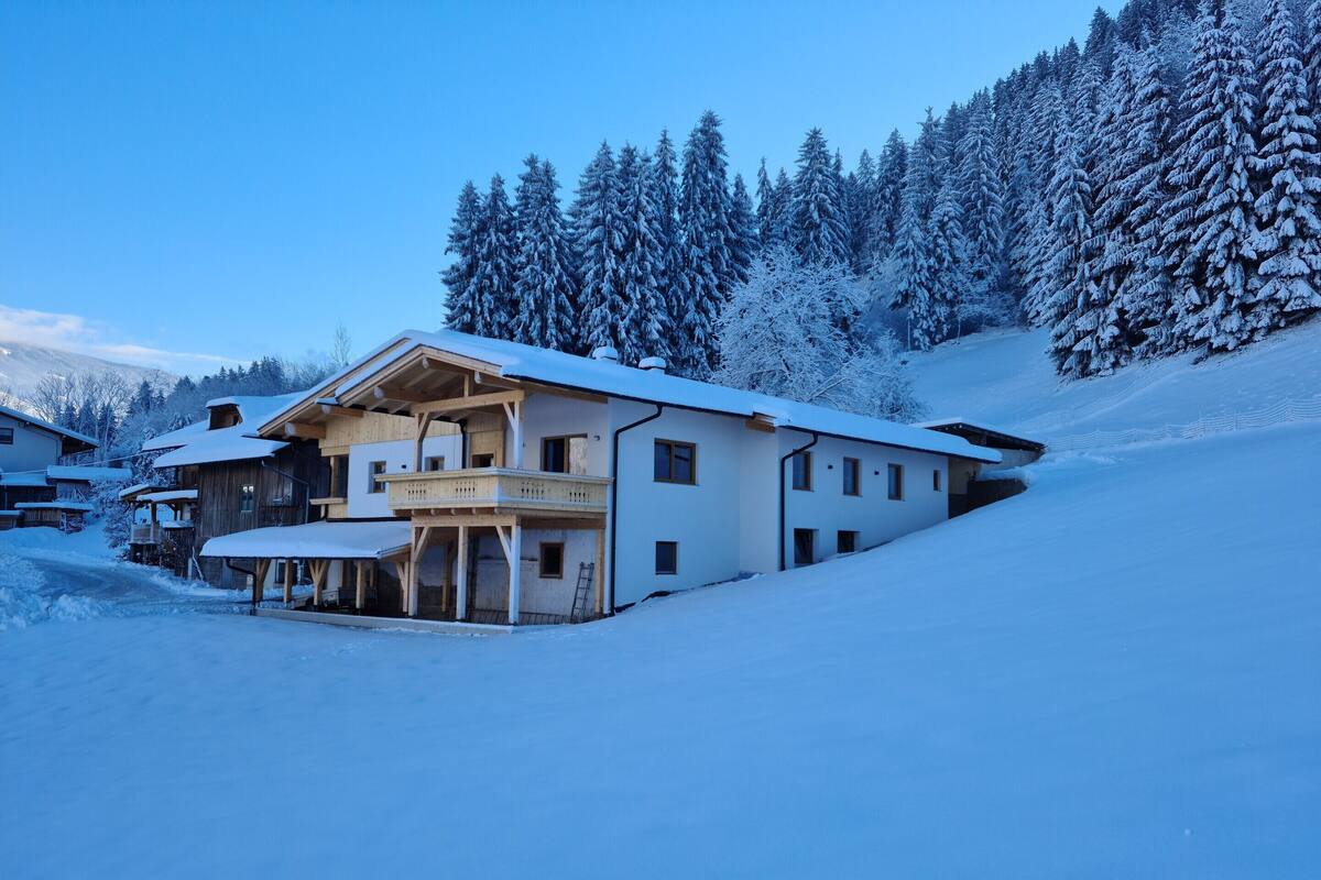 Un chalet enneigé doté de plusieurs pièces, d’un balcon et offrant une vue sur des arbres couverts de neige.