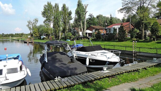 A calm canal with boats docked on wooden piers, surrounded by greenery and residential buildings. - Agriculture - Studios, Borzyslawiec by Lubczyna, Close to the Harbour (Goleniow)
