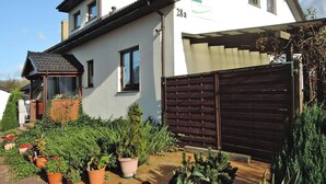 A two-story house with a white exterior, a brown roof, and a wooden fence. There are potted plants and a small garden area in front of the house. - Agriculture - Studios, Borzyslawiec by Lubczyna, Close to the Harbour (Goleniow)