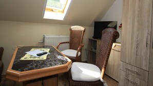 Une petite pièce avec un plafond en pente, une table avec des chaises, un téléviseur et un meuble.