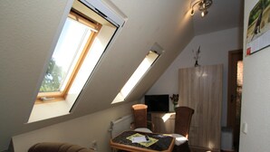 Une pièce mansardée chaleureuse, avec un plafond en pente, un canapé marron, une petite table à manger et un téléviseur.