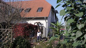 Une maison avec un toit recouvert de tuiles rouges, une clôture en bois et un jardin où poussent différentes plantes et fleurs.