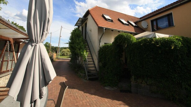 Un étroit sentier mène à une maison avec un toit en tuiles, un escalier et un espace extérieur abrité aménagé en coin salon.