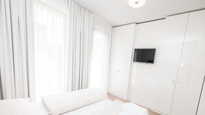 Quarto de hotel moderno com uma cama grande, uma televisão presa na parede e um guarda-roupa.