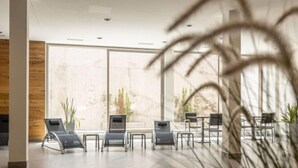 Espaço moderno em ambiente interno com poltronas e mesas, grandes janelas e plantas.