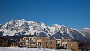 Um hotel moderno com vários andares e varandas, com as montanhas cobertas de neve ao fundo.