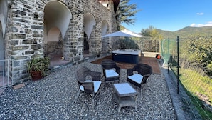 Una terrazza esterna con pareti in pietra, una vasca idromassaggio, mobili in vimini e vista sulle colline.