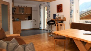 A cozy room with a wooden ceiling, a dining table with chairs, a sofa with cushions, a kitchen area with cabinets and a sink, and a window with a view of a building. - Apartment in Bramberg am Wildkogel With Parking Space (Bramberg am Wildkogel)