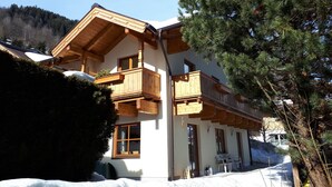 A two-story wooden chalet with balconies, a ski lift, and a snowy landscape. - Apartment in Bramberg am Wildkogel With Parking Space (Bramberg am Wildkogel)
