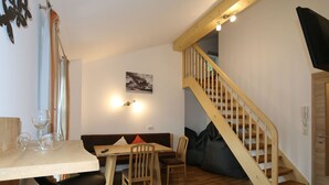 A dining area with a wooden table, chairs, and a sofa. There is a staircase with wooden railings leading to an upper level. - Apartment in Bramberg am Wildkogel With Parking Space (Bramberg am Wildkogel)