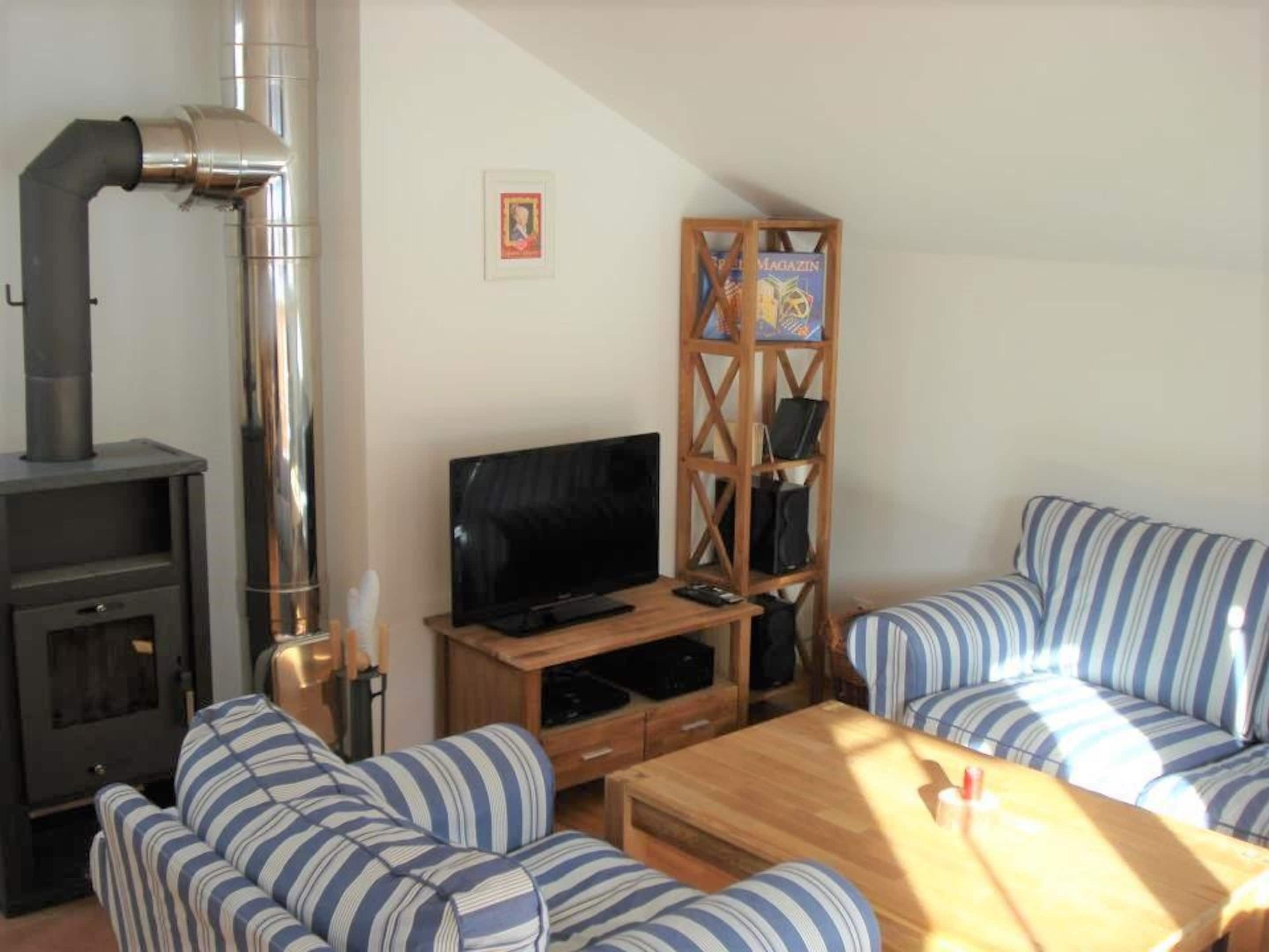Una sala de estar acogedora con chimenea, sofá a rayas, mesa de centro de madera y un mueble para televisión.