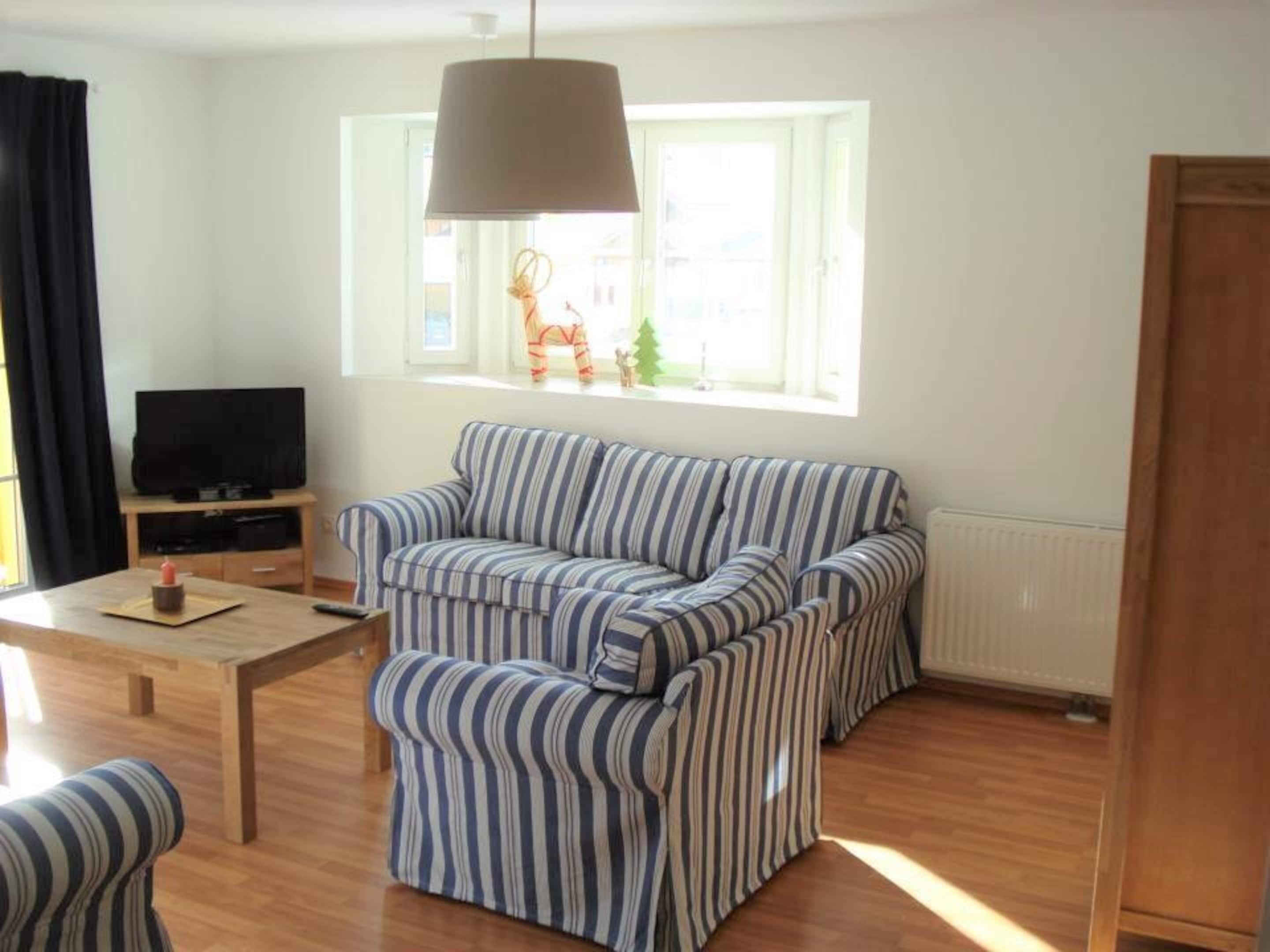 A living room with a striped sofa, a television on a wooden stand, and a window with a view of buildings.
