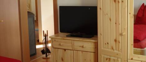 A bedroom with a wooden wardrobe, a television on top, and a red bedspread.