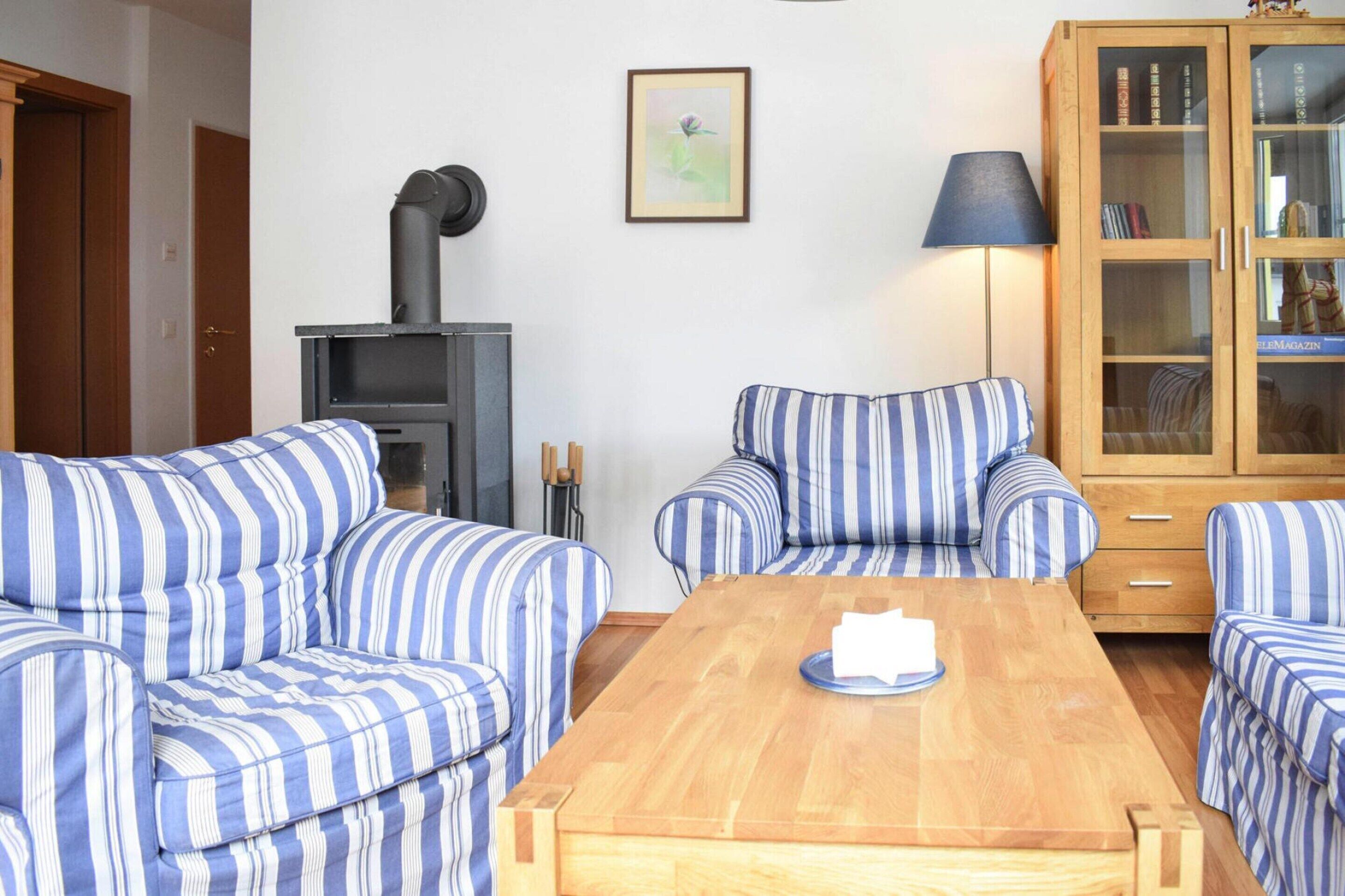 A room with striped blue and white sofas, a wooden coffee table, a cabinet with glass doors, and a fireplace.