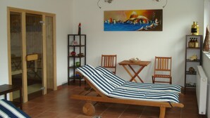 A room with a bed, a table, two chairs, a shelf with bottles, and a painting on the wall. - Villa in Altenmarkt With a Balcony (Altenmarkt im Pongau)