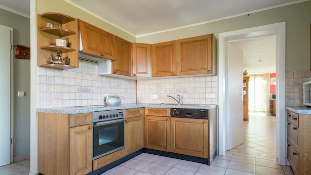A kitchen with wooden cabinets, a built-in oven, a dishwasher, and a granite countertop. - Spacious Holiday Home in Chodes With Sauna (Malmedy)
