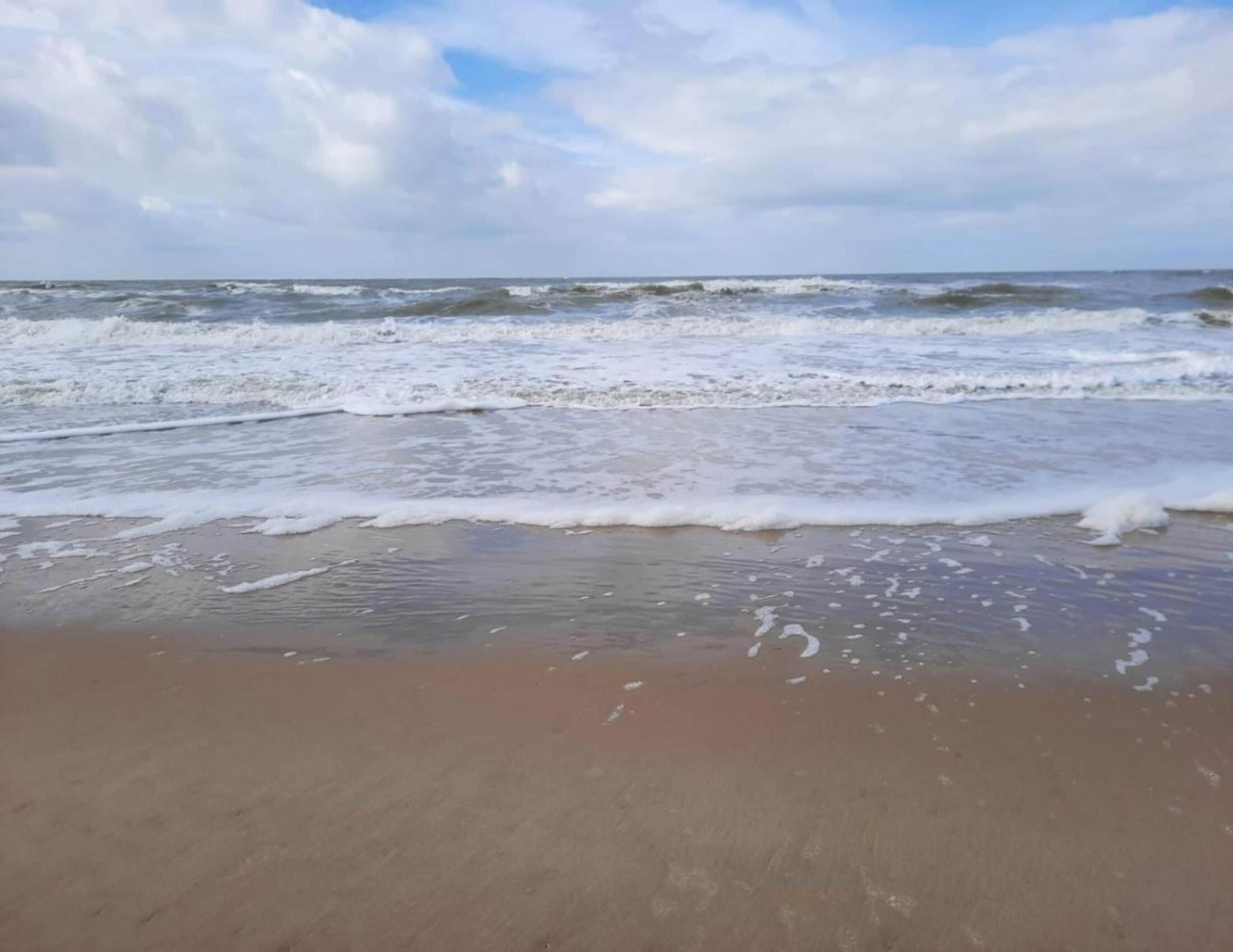 A beach with waves approaching the shore under a partly cloudy sky.