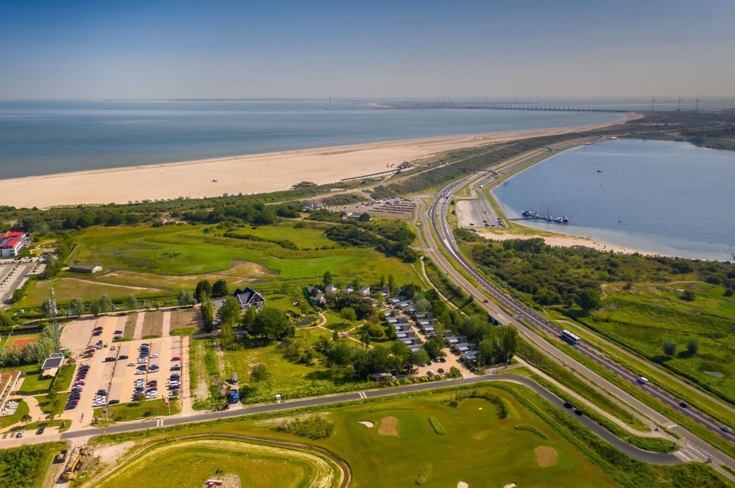 An aerial view of a coastal area with a highway, parking lot, and residential buildings.