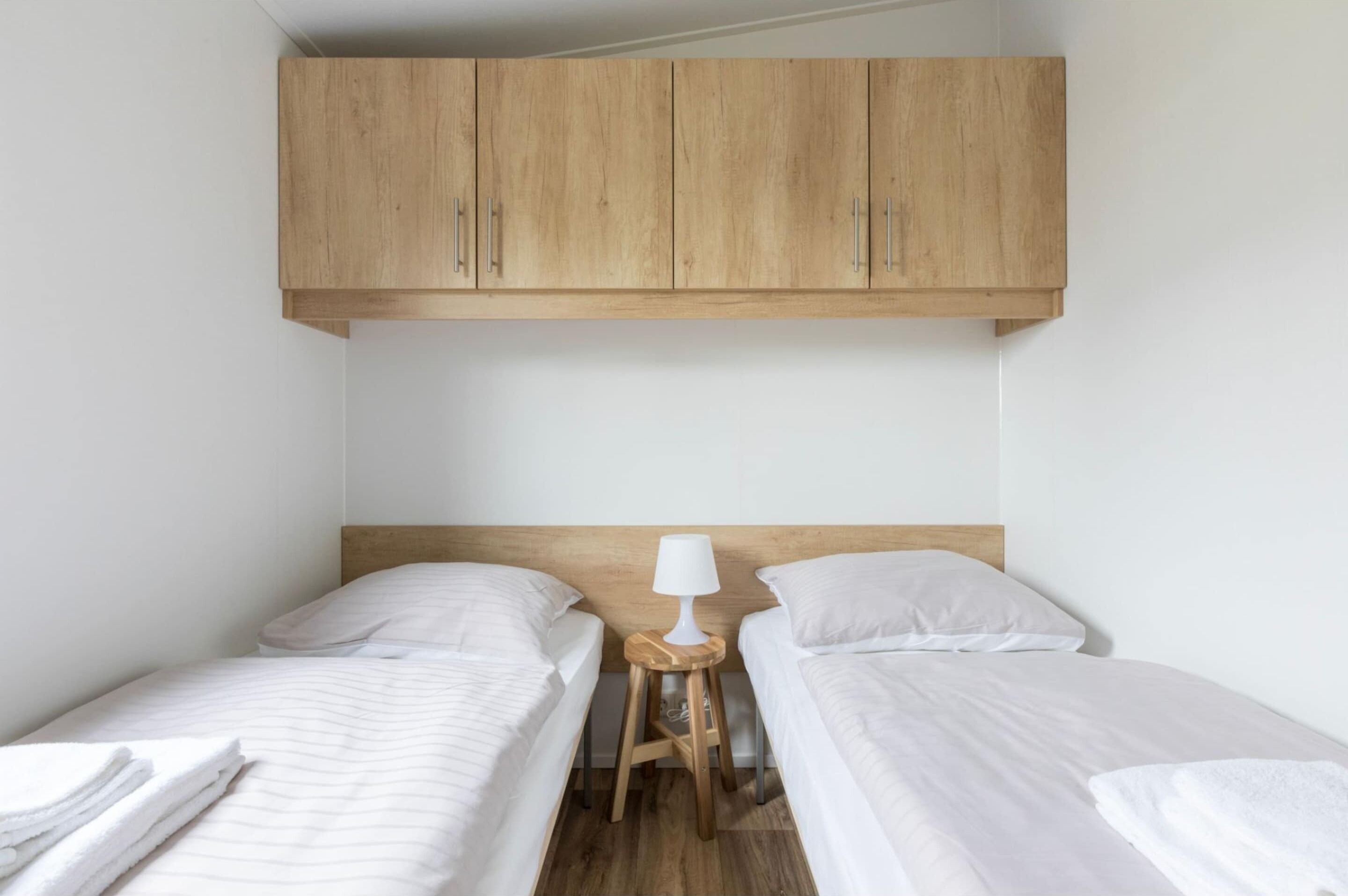 A small, clean room with two single beds, a wooden headboard, and a small table with a lamp.