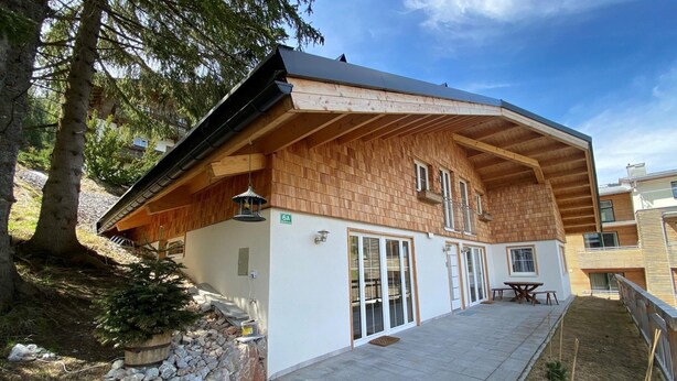 A two-story wooden house with a covered patio, stone pathway, and a small tree. - Chalet Salzburg, Dienten (Dienten am Hochkoenig)
