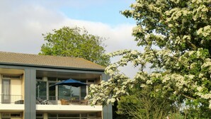 A two-story building with a balcony, outdoor seating, and a tree with white flowers. - Modern Apartment in Noordwijk Near the Sea (Noordwijk)