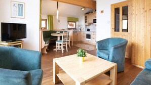 A cozy living room with a wooden coffee table, blue sofas, a television, and a kitchen in the background. - Holiday Flats Barlerhof, Konigsleiten (Wald im Pinzgau)
