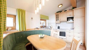 A cozy kitchen with a green upholstered bench, a round table with a bowl of flowers, and white cabinets. - Holiday Flats Barlerhof, Konigsleiten (Wald im Pinzgau)