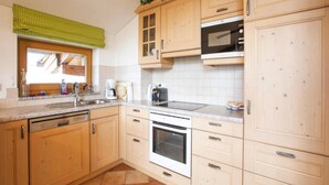 A kitchen with wooden cabinets, a built-in oven, a microwave, and a window with a green checkered blind. - Holiday Flats Barlerhof, Konigsleiten (Wald im Pinzgau)