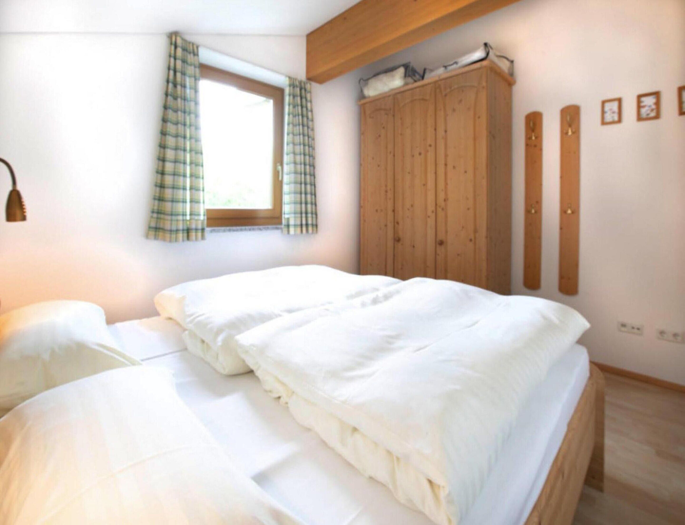 Ein Schlafzimmer mit Bett, einem Fenster mit Vorhängen, einem Kleiderschrank und einem an der Wand befestigten Regal.
