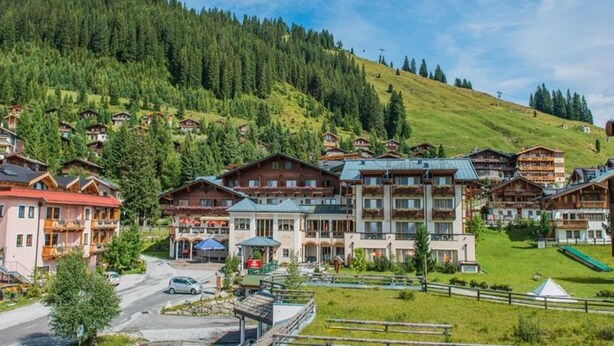 A mountain resort with chalet-style buildings, a parking area, and a view of a forested hill. - Holiday Flats Barlerhof, Konigsleiten (Wald im Pinzgau)
