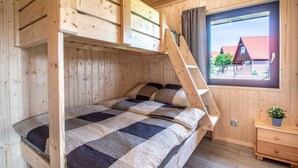 A wooden cabin bedroom with bunk beds, a window with a view of houses, and a small bedside table with a plant. - Chic Holiday Homes for up to 6 People in Ustka (Ustka)