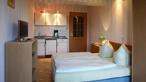 Habitación de hotel pequeña con cama, escritorio con computadora, kitchenette y puerta.
