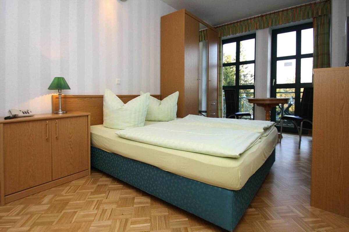A bedroom with a bed, wooden wardrobe, and a desk with a chair.