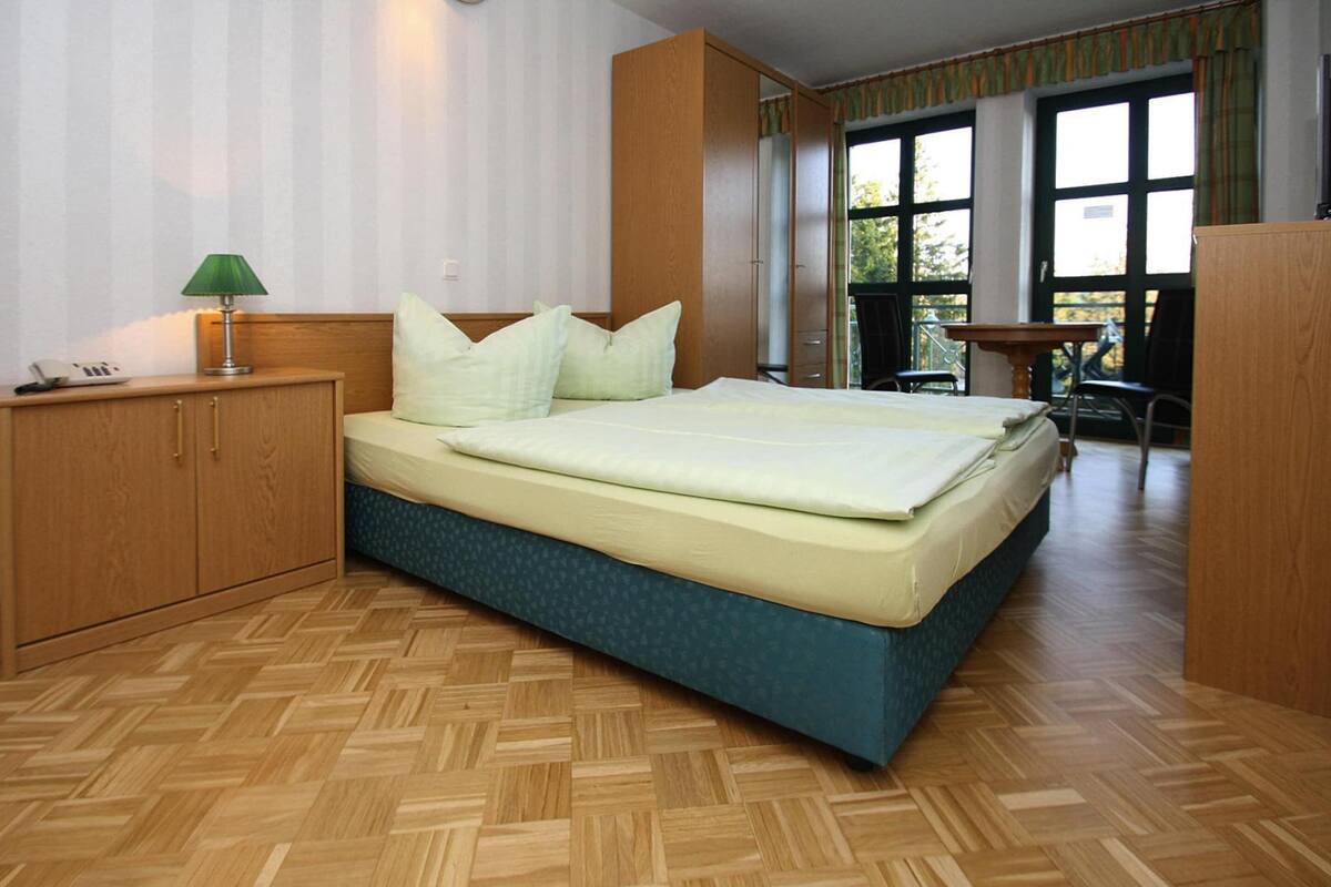 A bedroom with a bed, wooden wardrobe, and a desk with a lamp.