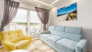 A room with a light blue sofa, a yellow armchair, and a large window with curtains. - Modern 2-room Apartment in the new Apartment Complex, Grzybowo (Kołobrzeg)